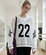 Dancer wearing a white sweater with black 22 numbers and stars on sleeves in an dance studio