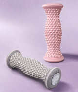 Two textured Covet Dance Arch Angel massage rollers, one pink and one gray, on a light purple background.