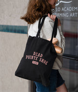 A woman wearing a light gray sweatshirt and denim shorts carries a black canvas tote bag with pink text reading 'DEAD POINTE SHOE CLUB' entering a dance studio.