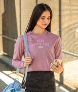 Dancer in a pink long-sleeve shirt with Dead Pointe Shoe Club design, holding a blue bag and phone, walking outside.