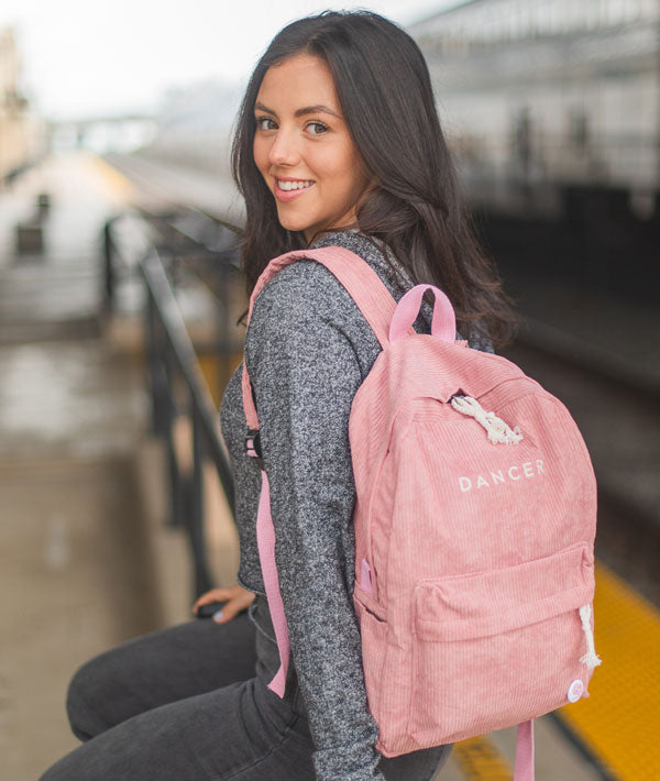 Kira waiting for the train with her Dancer Embroidered Backpack in rose pink color
