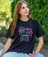 Dancer wearing a black t-shirt with "Notes to Self-Daily Dance Reminders" printed on it, sitting outdoors.