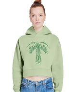 A bunhead model wearing a light sage green cropped hoodie with a dark green graphic of a mistletoe andholly garland with the cursive text 'pointe your mistletoes', paired with blue jeans against a plain white background.