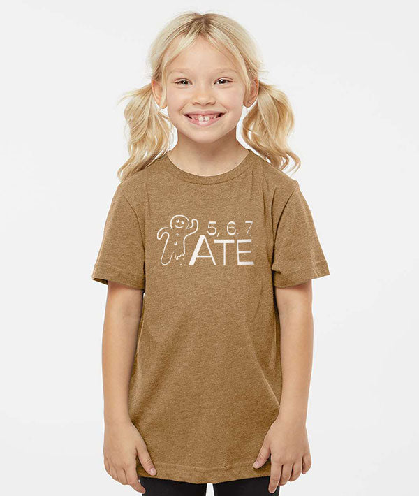 Young girl wearing an orange brown t-shirt depicting a Gingerbread man, and text that says "5, 6, 7, ATE"