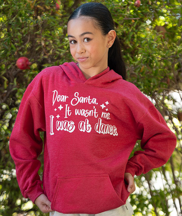 Young ballerina wearing a red hoodie with "Dear Sant, It wasn't me. I was at dance" in front of a pomegranate tree