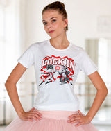 A ballet dancer modeling a white short-sleeve graphic t-shirt with a red and black 'LOCK IN'' Nutcracker vs. Mouse King design, paired with a light pink tutu skirt in a bright indoor studio setting.