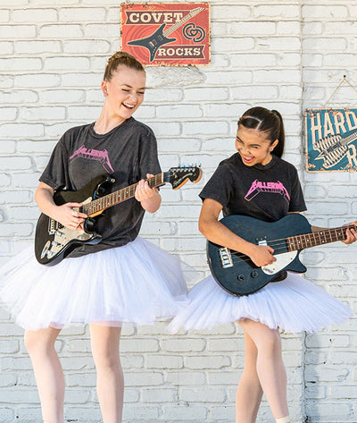 Two young girls playing electric guitars in front of a white brick wall with Covet Rocks decor wearing vintage band tees with pink Ballerina graphic