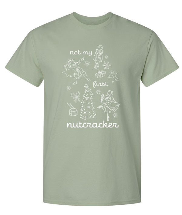 Light green tee shirt that says "Not my first nutcracker" in white print, and depicts the Nutcracker, Mouse King, Clara doing ballet in pointe shoes, and Christmas themed items: snowflakes, candy canes, a drum, a Christmas tree, a wrapped present, and a gingerbread man.