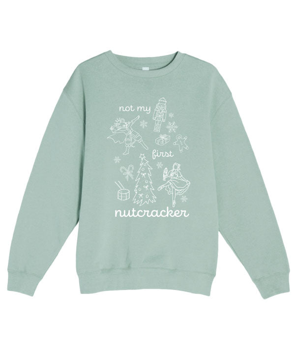 Light green sweatshirt that says "Not my first nutcracker" in white print, and depicts the Nutcracker, Mouse King, Clara doing ballet in pointe shoes, and Christmas themed items: snowflakes, candy canes, a drum, a Christmas tree, a wrapped present, and a gingerbread man.