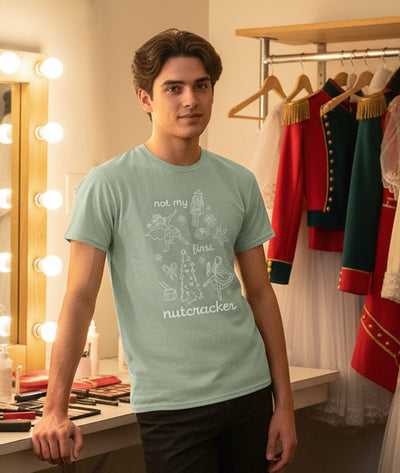 Male dancer wearing a light green t-shirt with 'Not My First Nutcracker' design backstage in a dressing room.