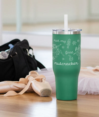 Green 40 oz. tumbler with 'not my first nutcracker' design on a wooden dance studio floor with ballet pointe shoes and a dance bag.