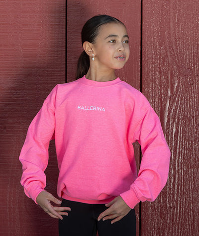 young dancer wearing a bright pink sweatshirt with 'BALLERINA' embroidered on it