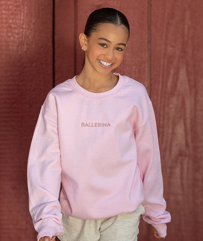 Dancer wearing an embroidered pink 'BALLERINA' sweatshirt against a red-brown background