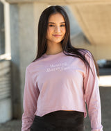 Ballerina with her hair down wearing a light pink long-sleeve shirt with Resting Barre Face on it, standing outdoors.