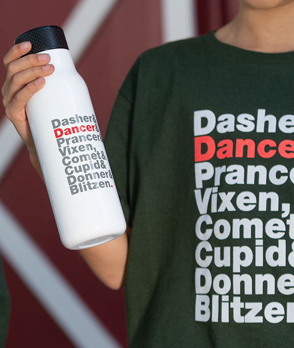 Person wearing a Reindeer Names tee and holding a white water bottle with all the reindeer names in grey text except for DANCER in red