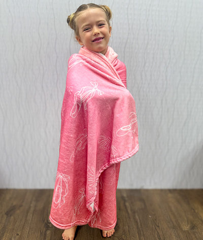 Child wrapped in a pink hooded blanket with white pointe shoes and tutu illustrations on a plain background